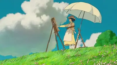 A young woman paints under a parasol in a grassy field