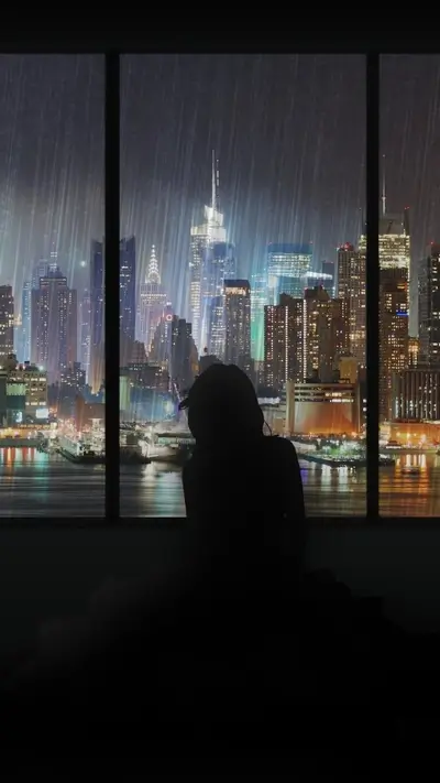 Silhouette of a person looking at a rainy city at night
