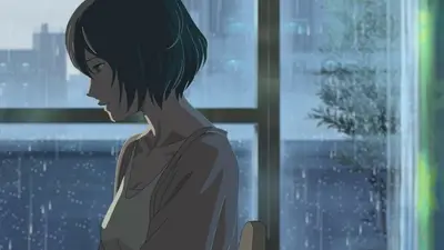 Woman sitting indoors near rainy window looking down